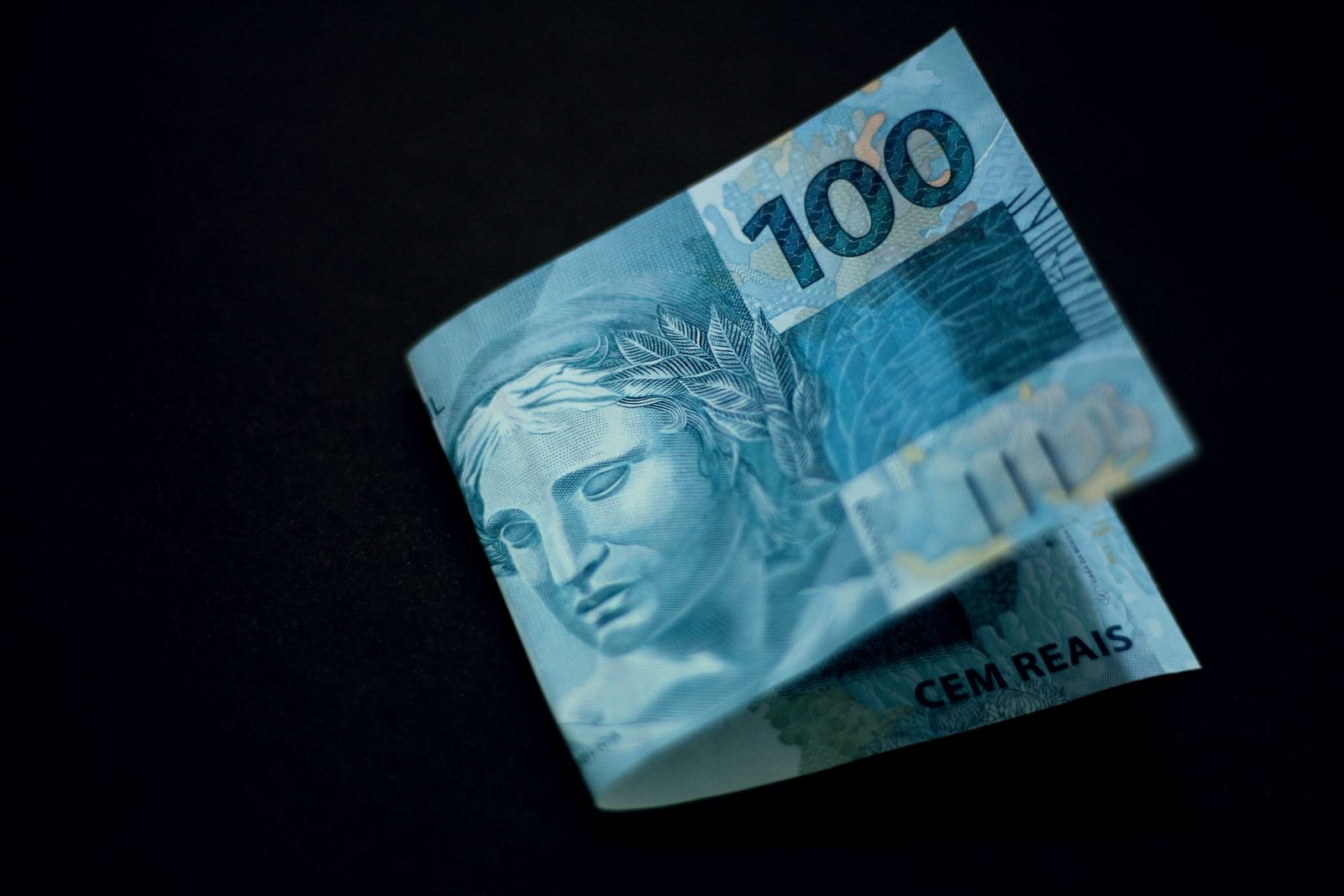 Cédula de 100 reais dobrada sobre fundo preto