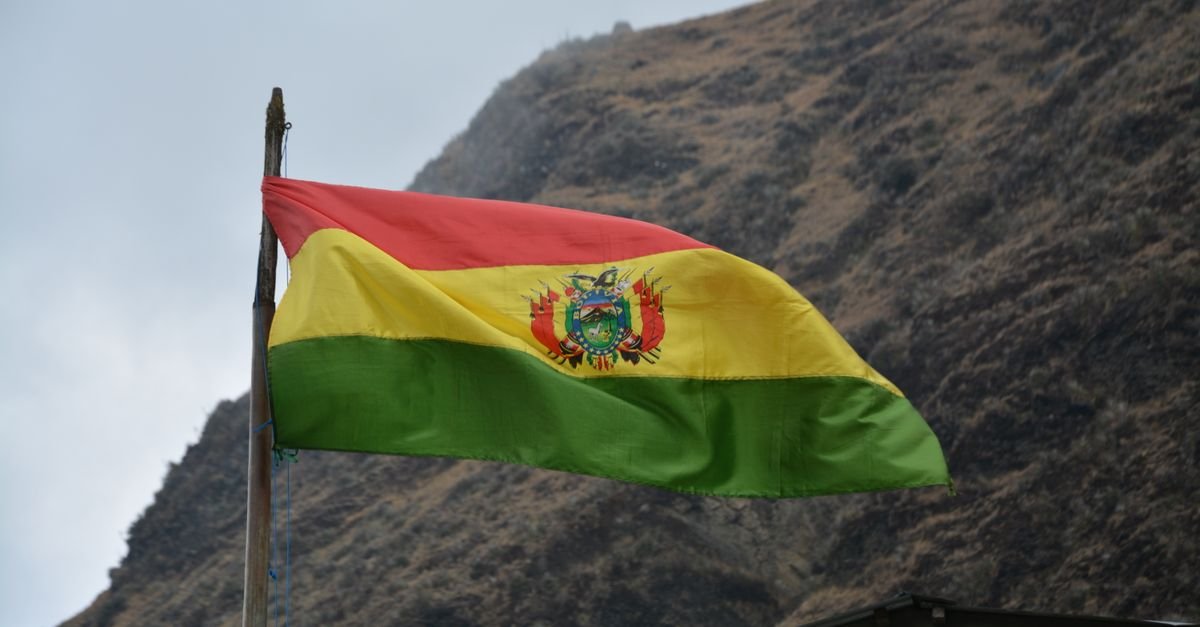 Bandeira da Bolívia hasteada, com encosta de montanha ao fundo