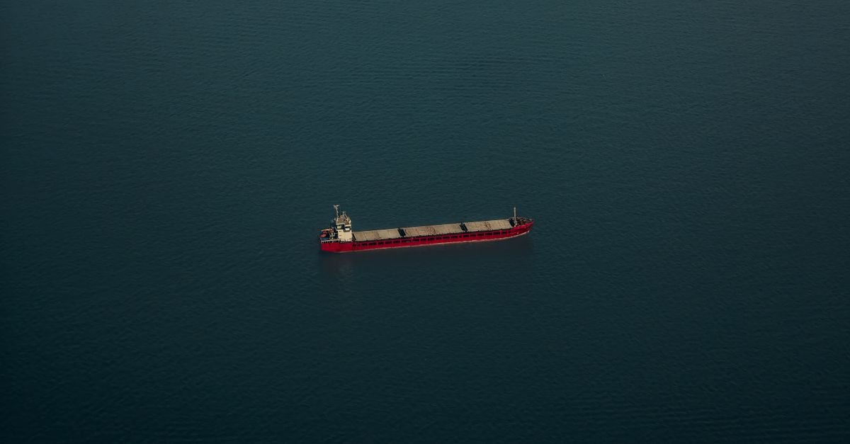 Navio graneleiro de casco vermelho navegando sozinho em mar aberto, visto do alto