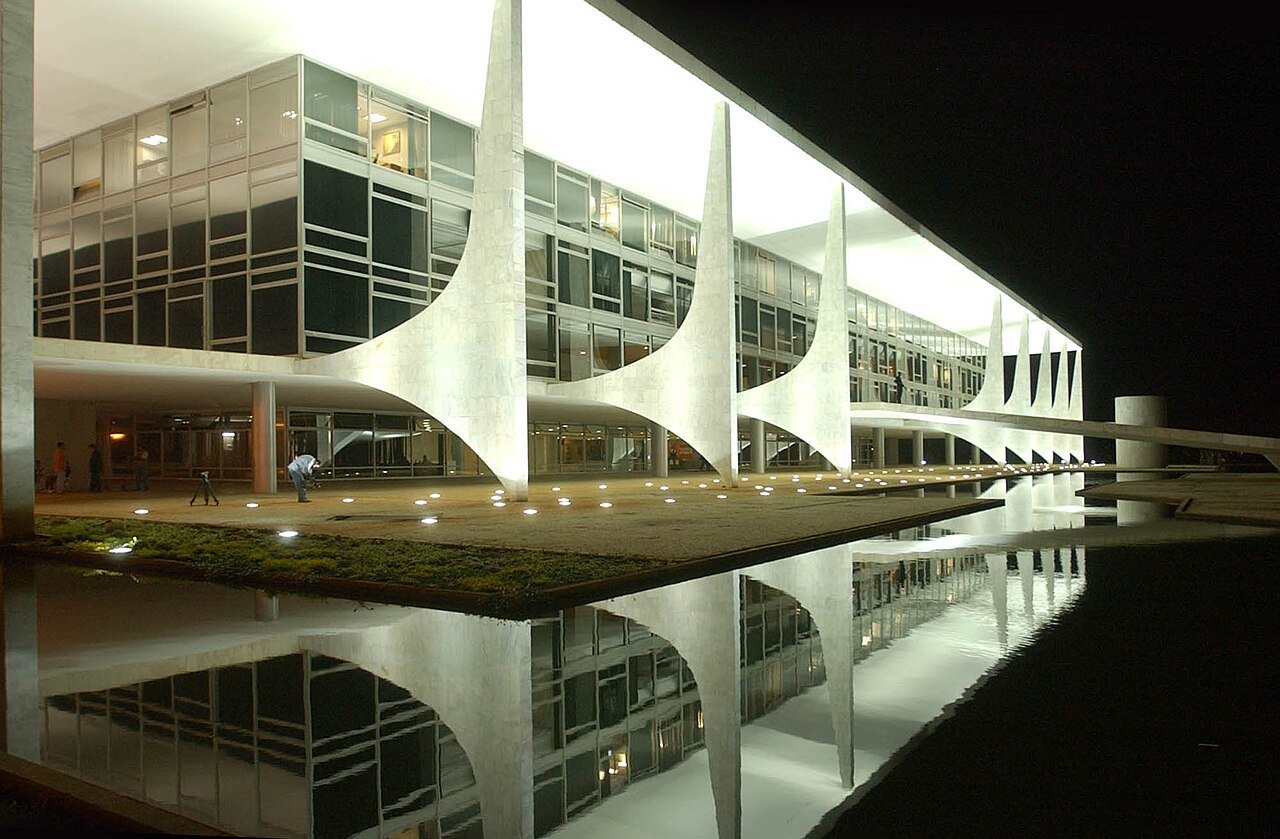 Fachada do Palácio do Planalto iluminada à noite, com o espelho d'água em primeiro plano