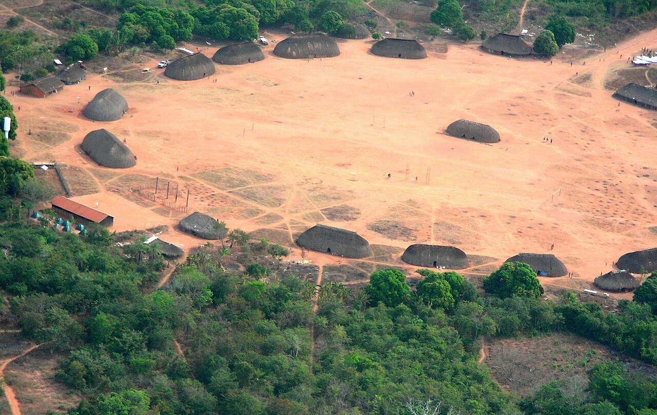 Vista aérea de aldeia no Parque Indígena do Xingu, com ocas dispostas em círculo em torno de pátio de terra