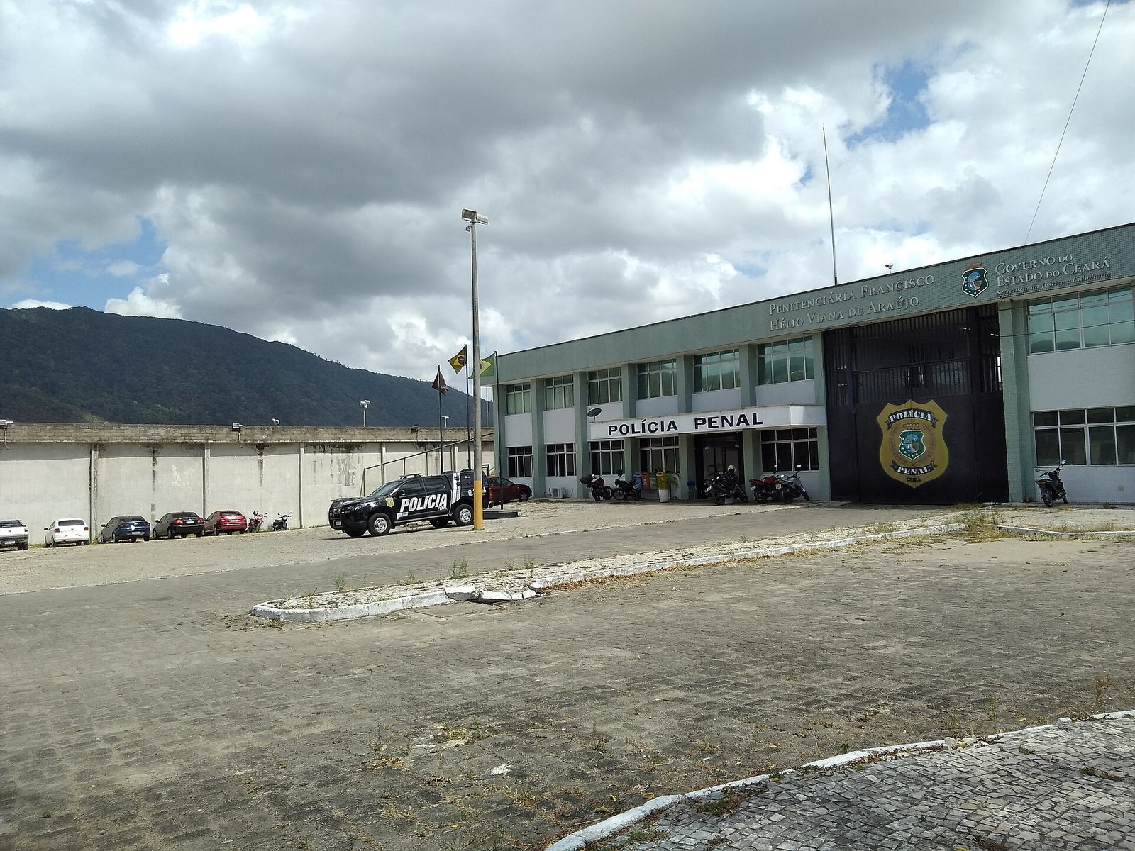 Fachada externa de unidade prisional brasileira, com muro, guarita e viatura da Polícia Penal