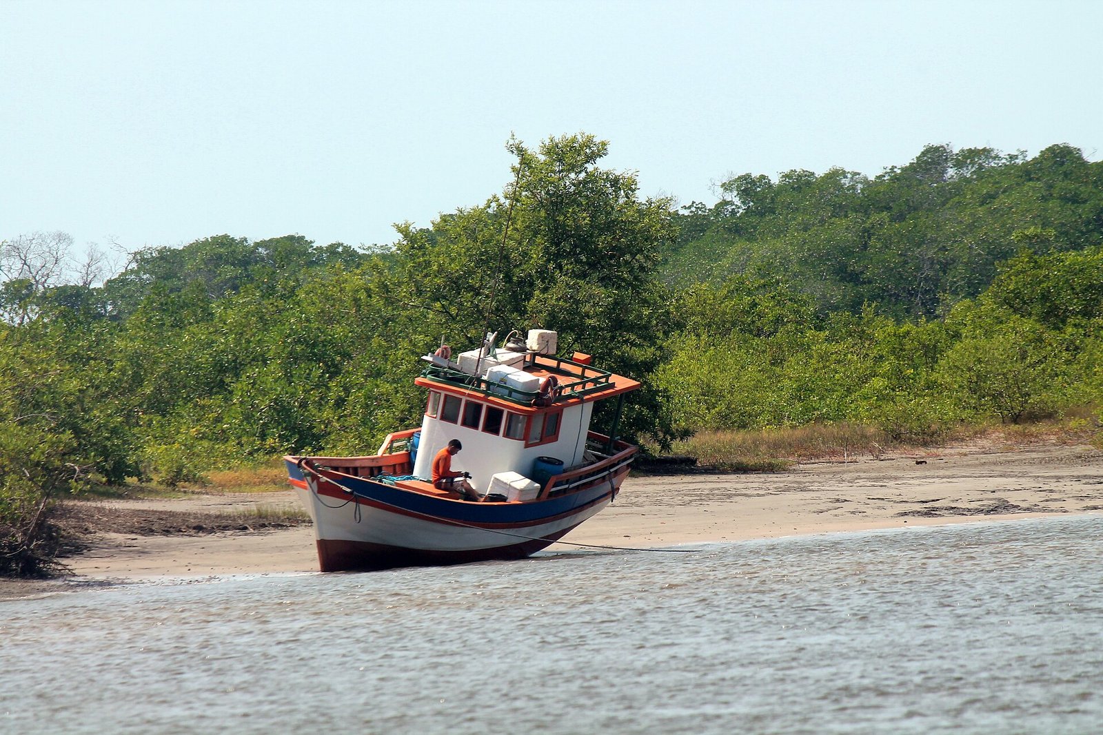 Barco de pesca de madeira encalhado na margem arenosa de rio cercado por mangue no Brasil