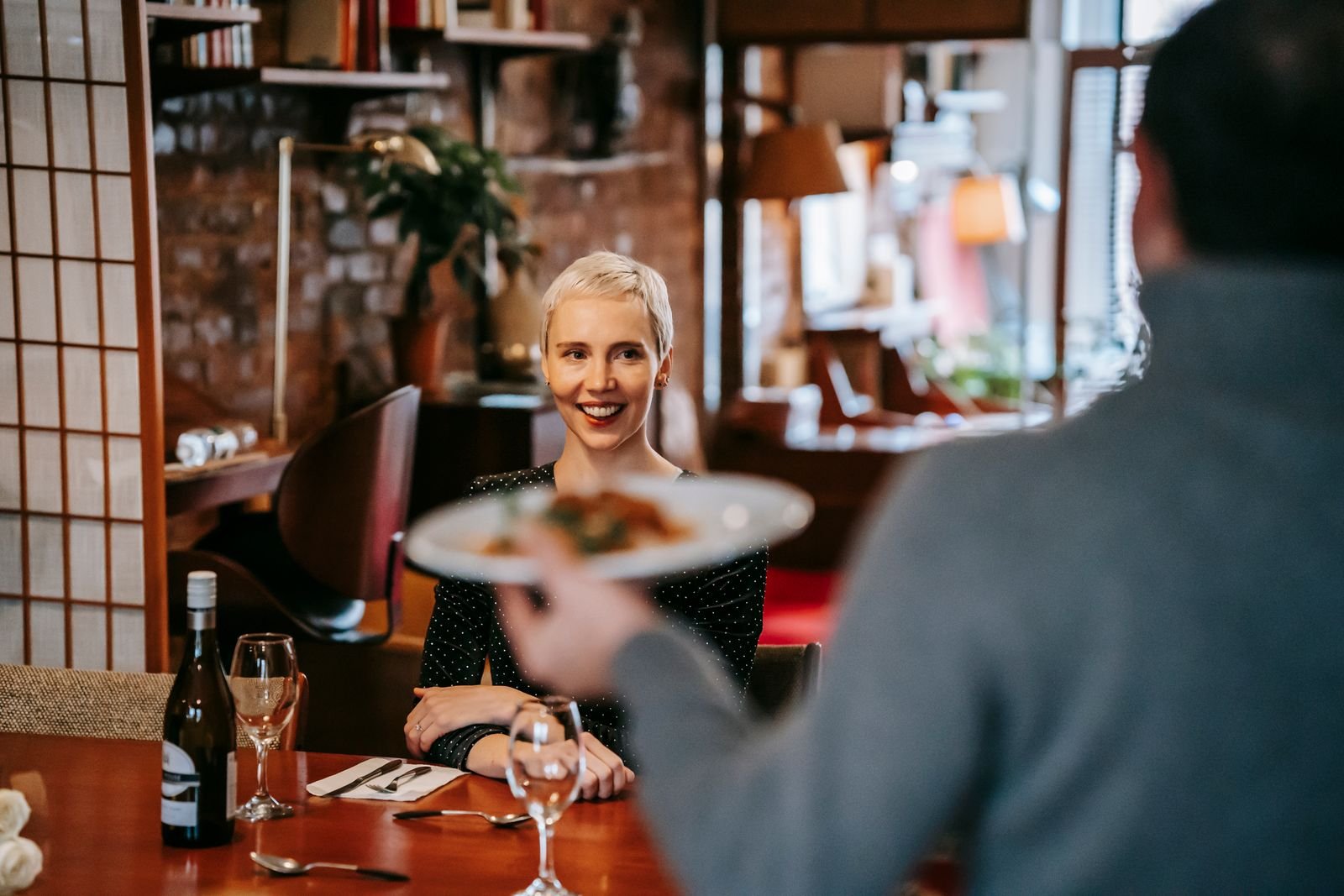 Garçom serve prato a cliente sorridente em restaurante, em foto de arquivo