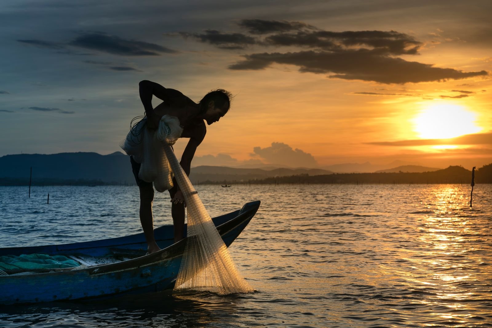 Pescador em silhueta lança rede de uma canoa ao entardecer
