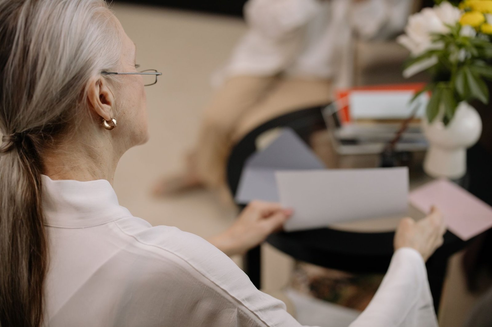 Mulher idosa de cabelo grisalho separa folhas de papel sobre uma mesa (foto ilustrativa de banco de imagens)