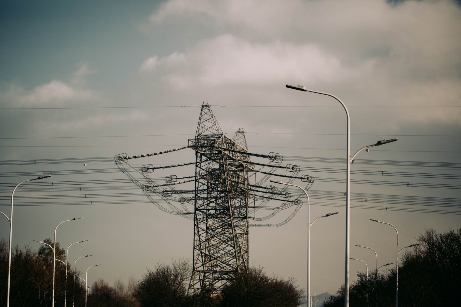 Torre de transmissão de energia elétrica e postes de iluminação sob céu nublado