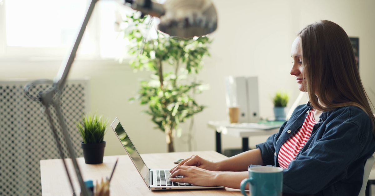 Mulher sentada à mesa de escritório digitando em um notebook