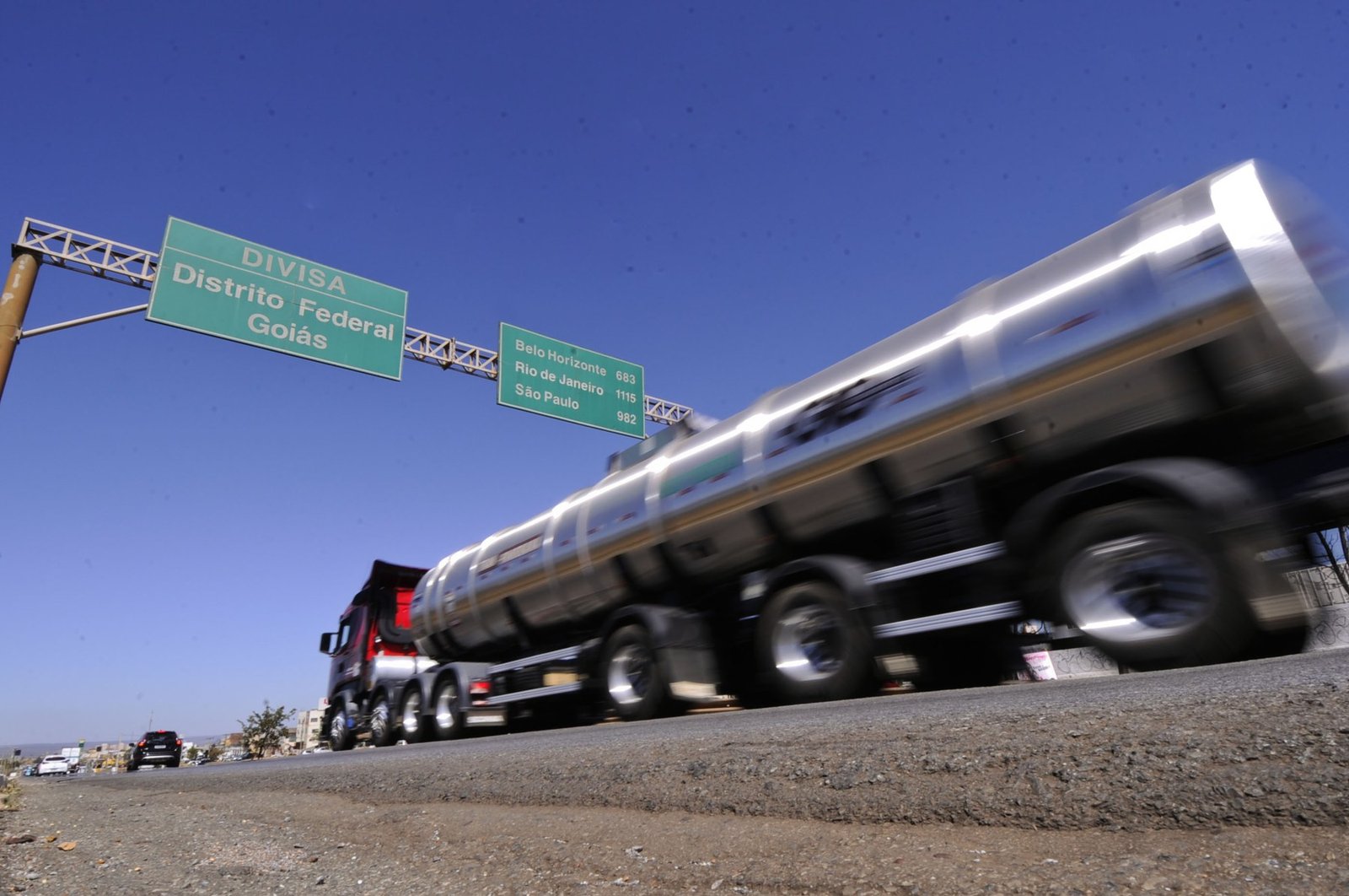 Caminhão-tanque em movimento sob placa de divisa entre o Distrito Federal e Goiás
