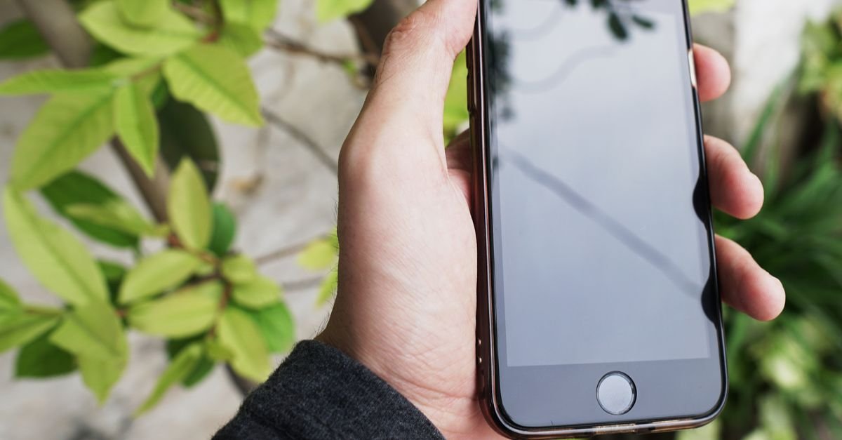 Mão segurando um telefone celular com a tela desligada