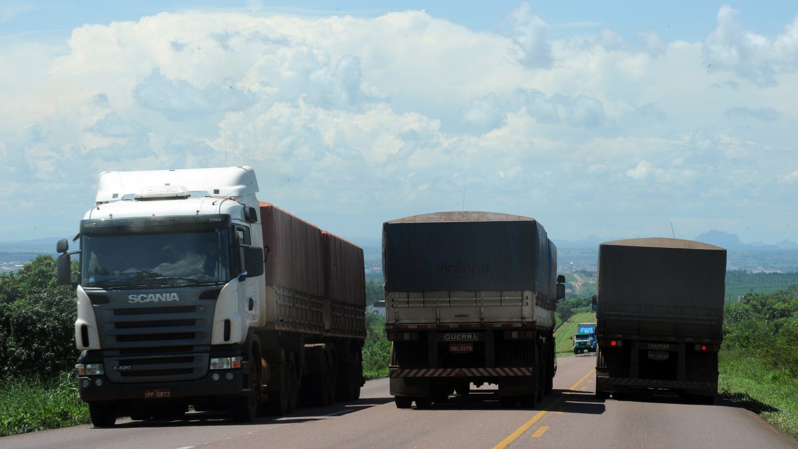 Três caminhões graneleiros carregados trafegam em rodovia de pista simples em Rondonópolis, no Mato Grosso