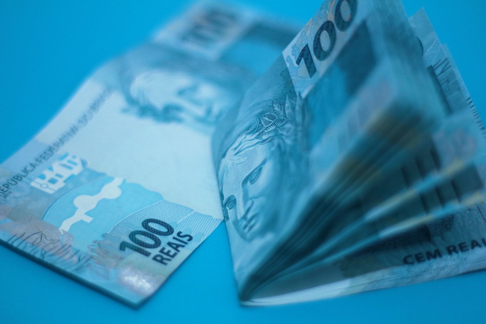 Cédulas de 100 reais empilhadas sobre superfície azul