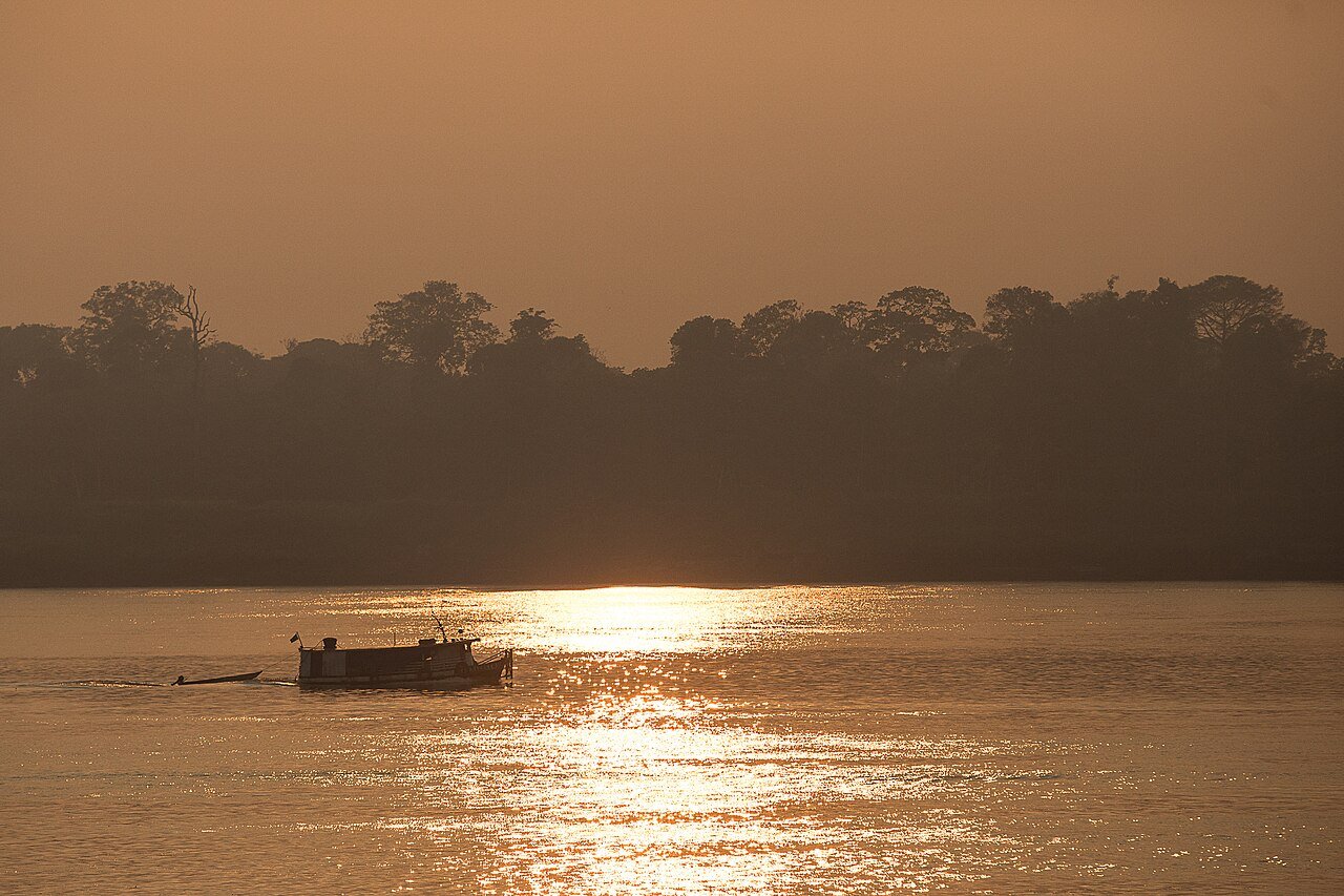 Barco navega em rio sob céu alaranjado de fumaça, com a floresta ao fundo, em foto de arquivo de 2020
