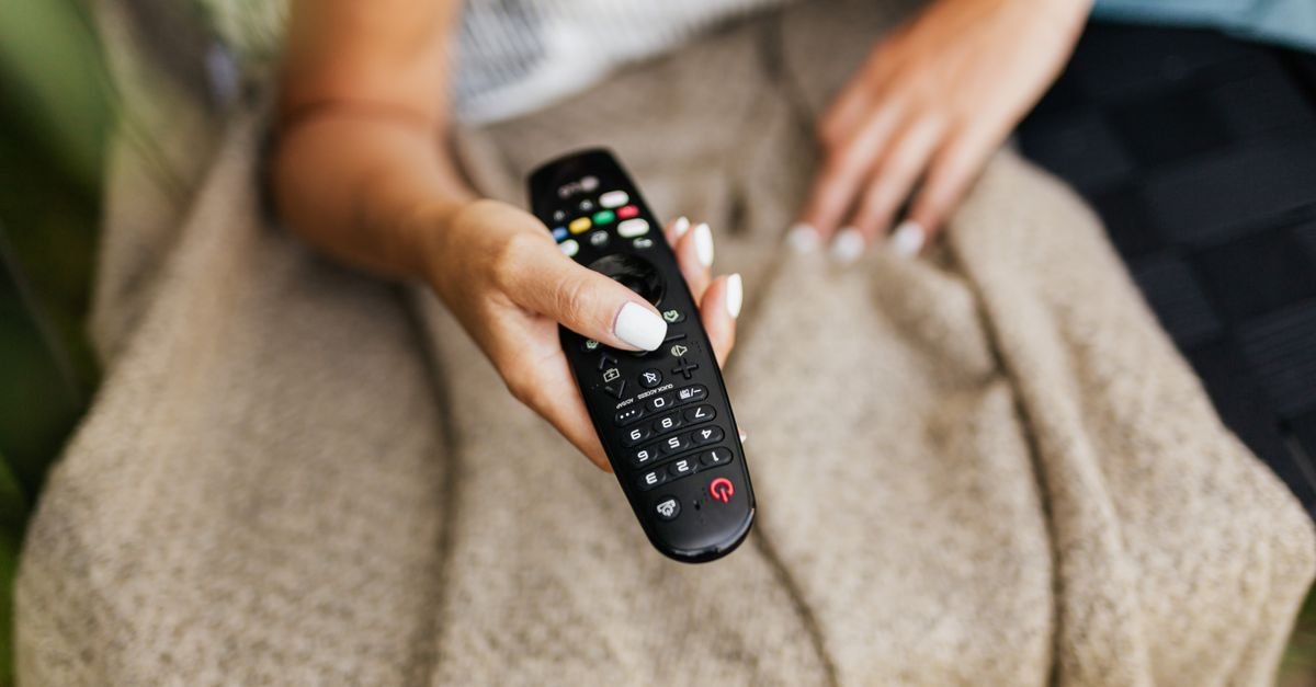 Mão segurando um controle remoto de televisão, imagem ilustrativa