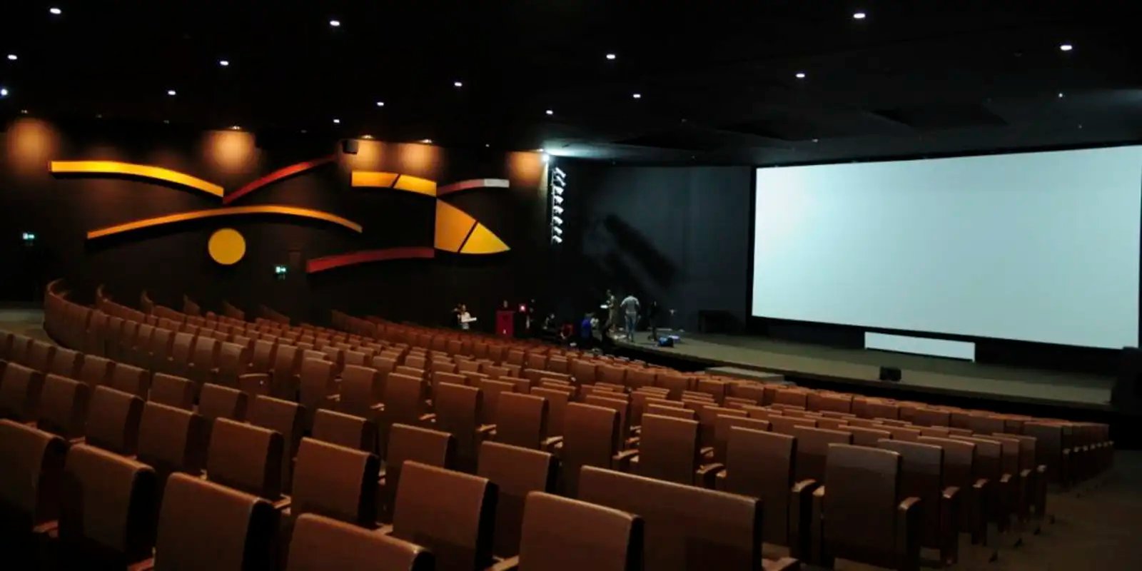 Sala de cinema vazia com poltronas marrons voltadas para a tela