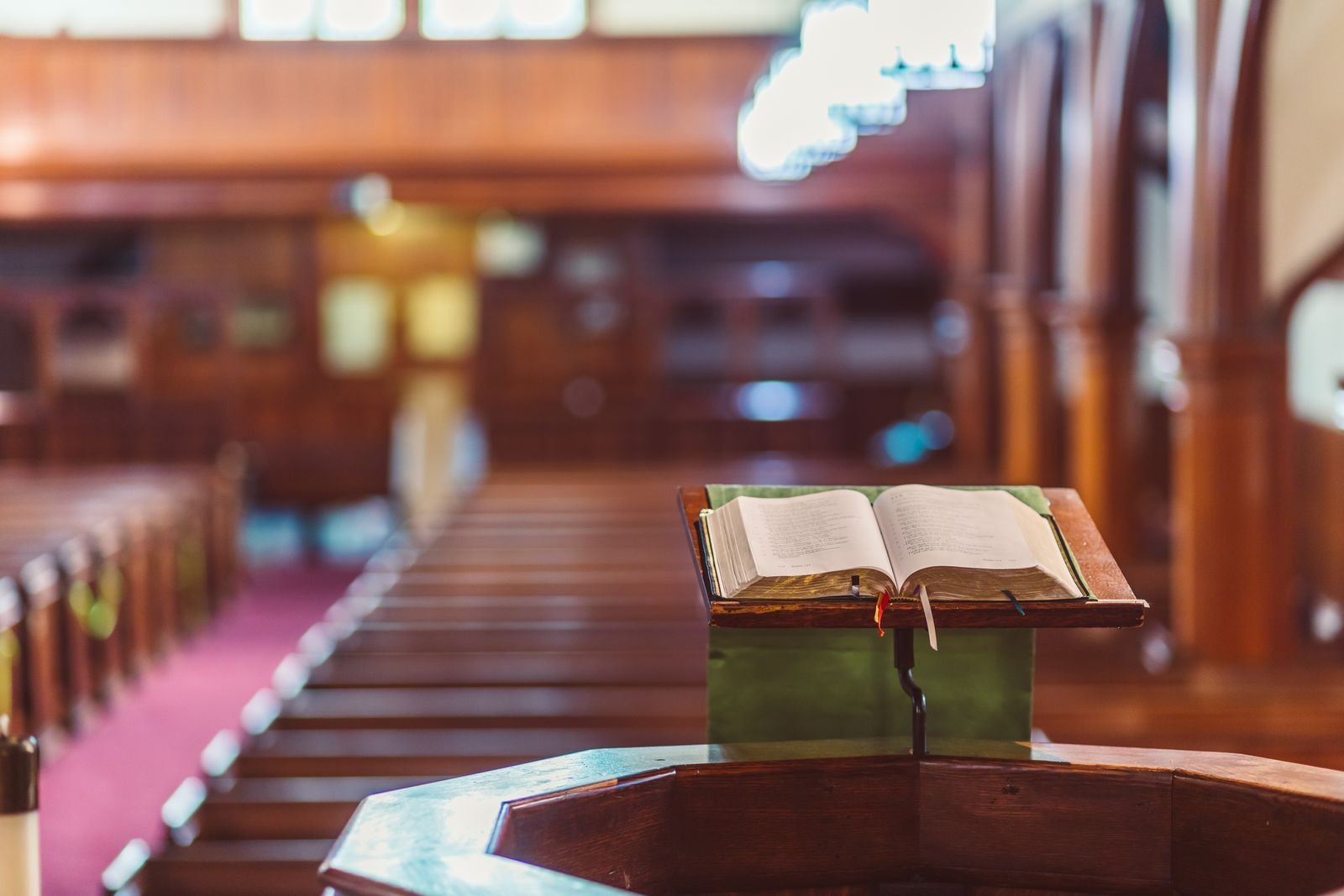 Bíblia aberta sobre um púlpito de madeira em uma igreja, com bancos ao fundo