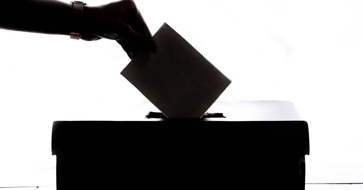 Mão deposita cédula em urna de votação, em silhueta