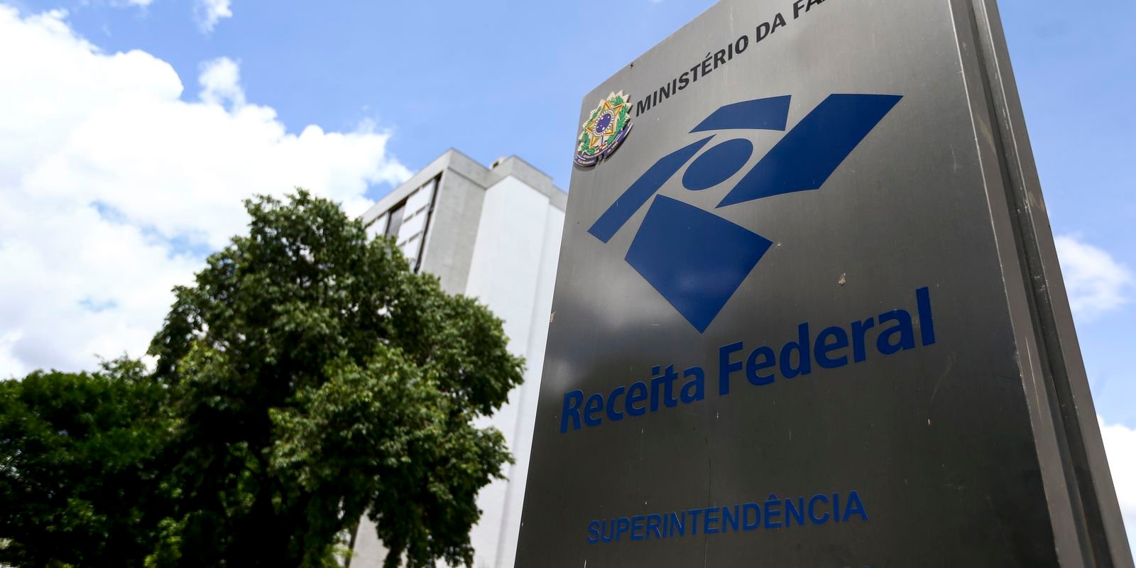 Placa metálica da Receita Federal e do Ministério da Fazenda em frente a prédio