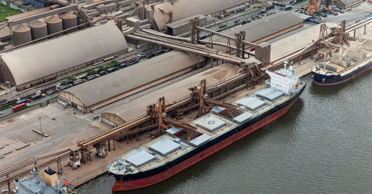 Vista aérea de navio graneleiro atracado em porto brasileiro com silos e correias transportadoras