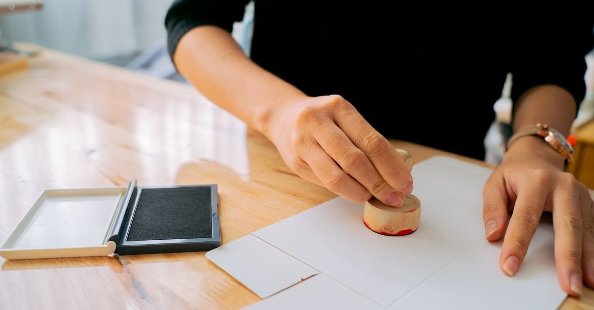 Mãos aplicando um carimbo sobre documento em uma mesa de madeira