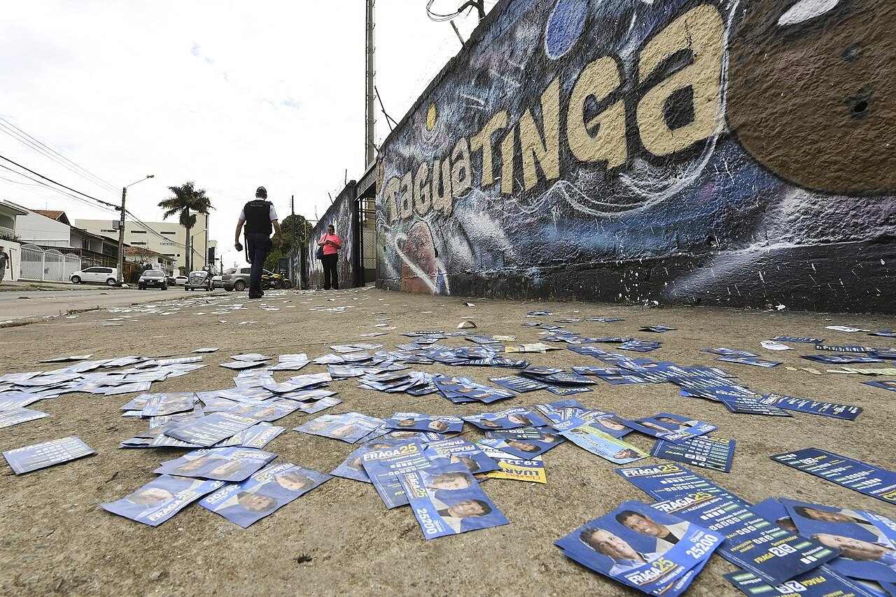 Santinhos de candidatos espalhados na calçada junto a um muro grafitado com a palavra Taguatinga, no DF, no primeiro turno de 2018 (foto de arquivo)