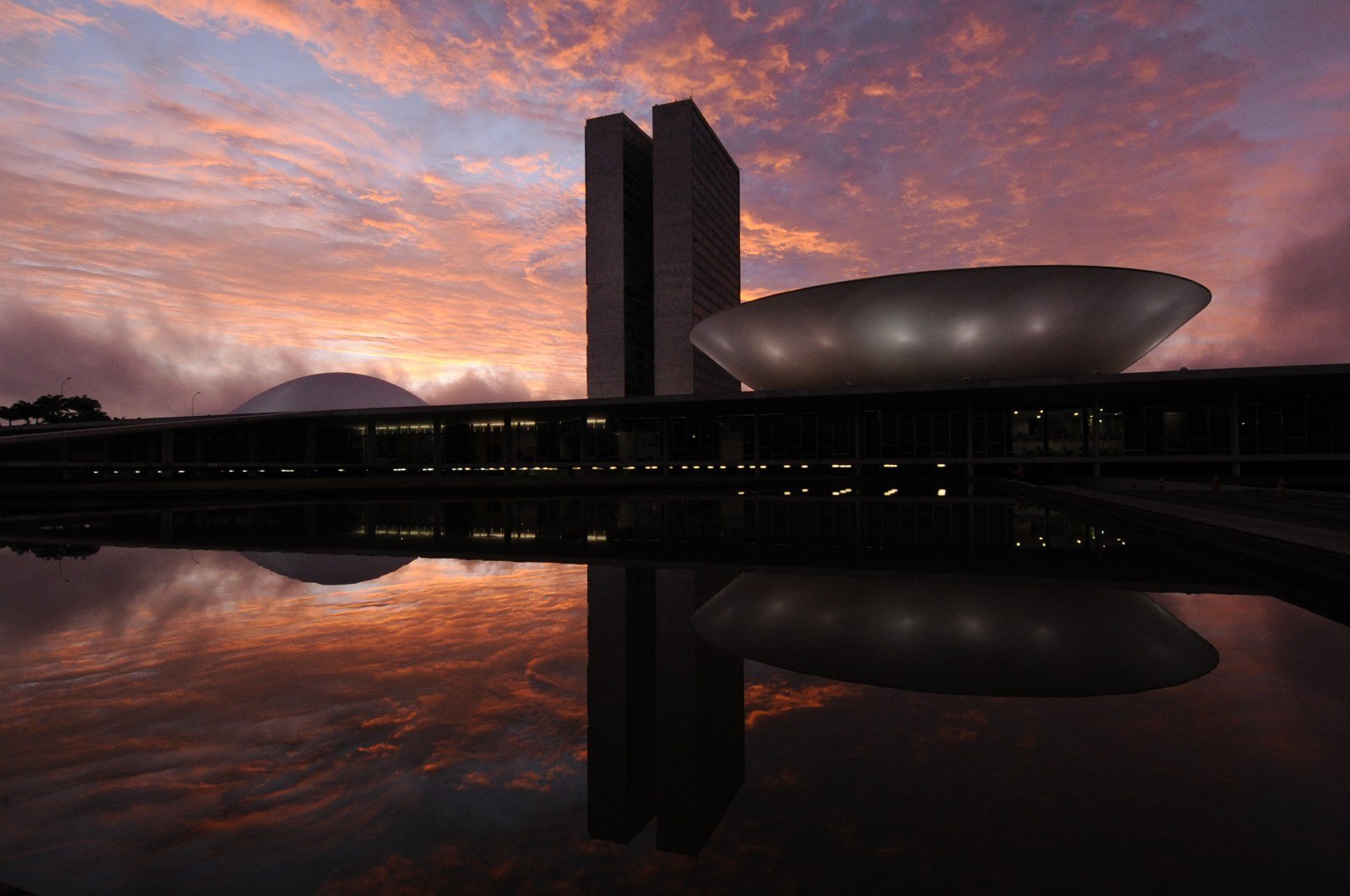 Congresso Nacional ao amanhecer, com céu alaranjado e reflexo no espelho d'água, em Brasília (foto de arquivo)