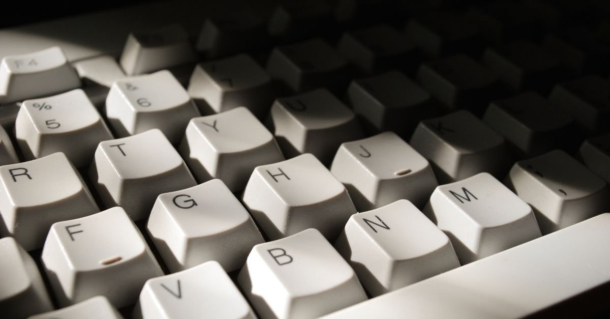 Close de teclado de computador branco com as teclas de letras em destaque sob luz lateral