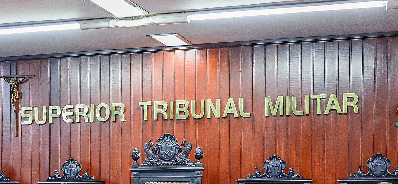 Letreiro Superior Tribunal Militar em parede de madeira do plenário, ao lado de crucifixo e das cadeiras dos ministros