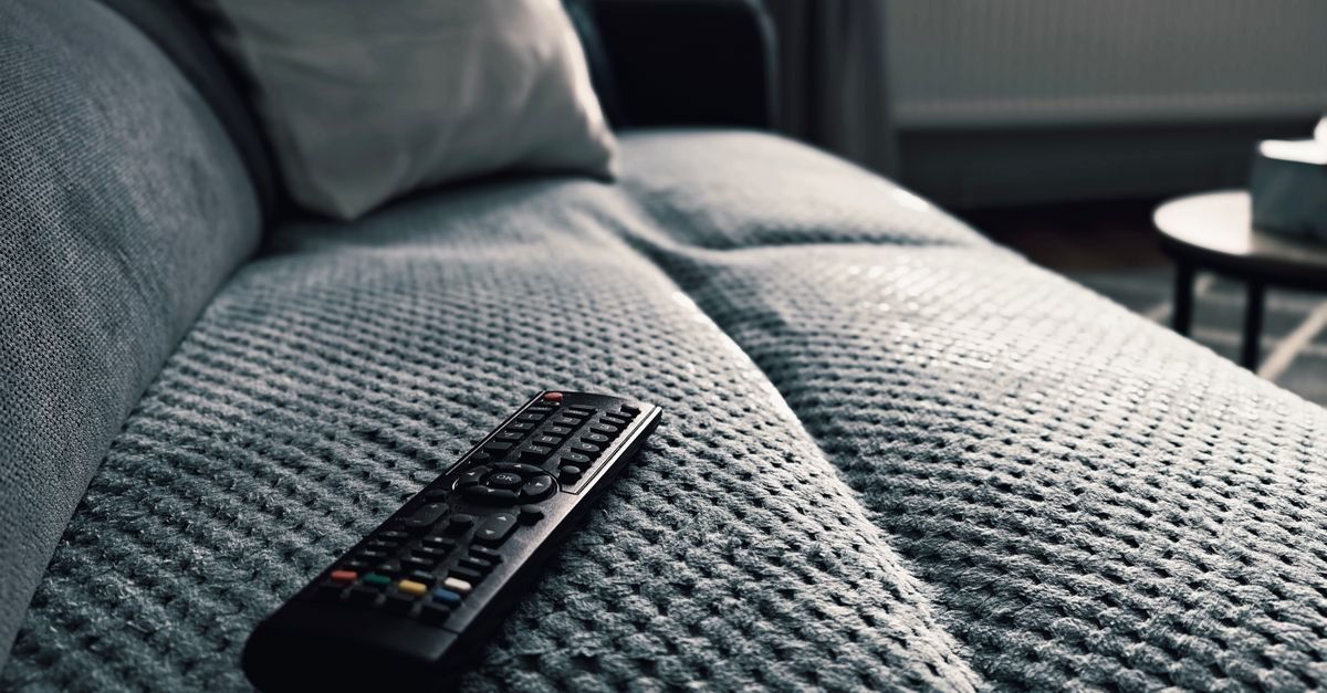 Controle remoto de televisão sobre manta de sofá em sala de estar com luz baixa