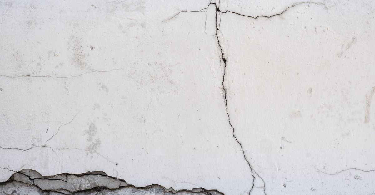Parede de concreto com rachadura vertical e reboco solto na base