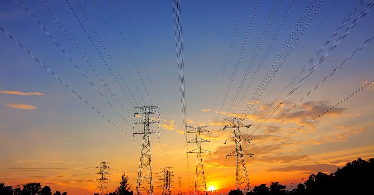 Torres de transmissão de energia elétrica em silhueta contra o céu no fim da tarde