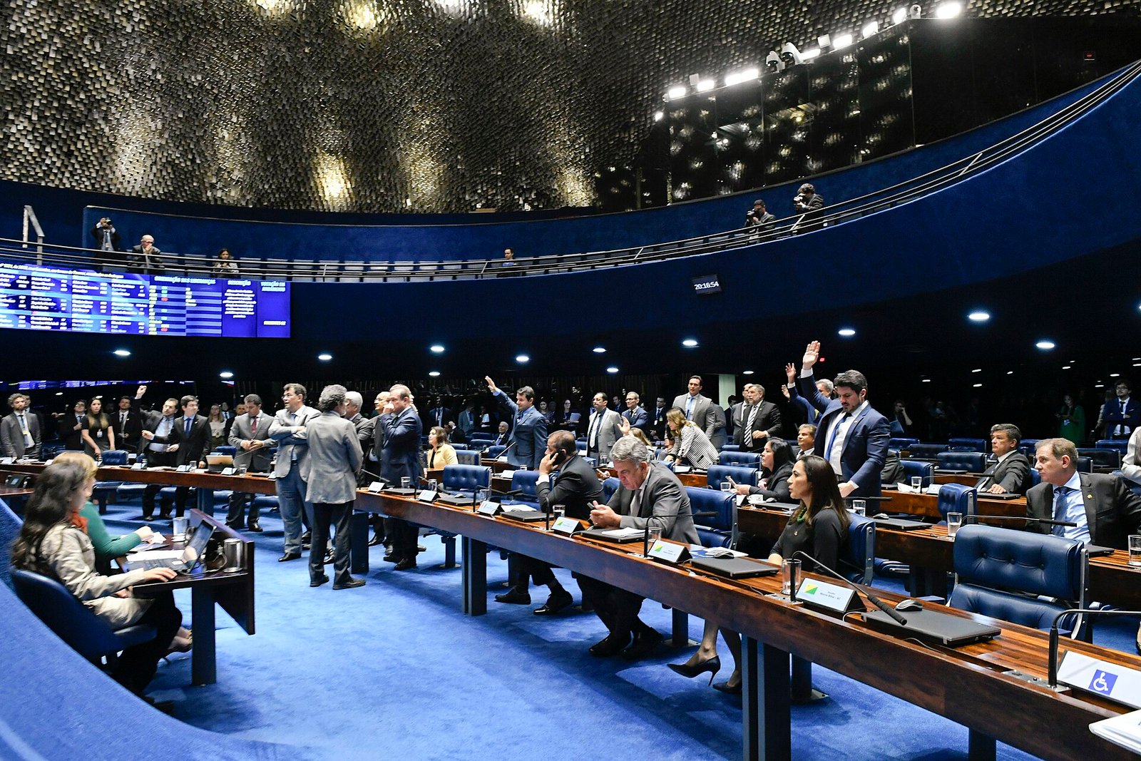 Plenário do Senado Federal em plano aberto durante sessão deliberativa, com senadores nas bancadas e alguns de braço erguido em votação