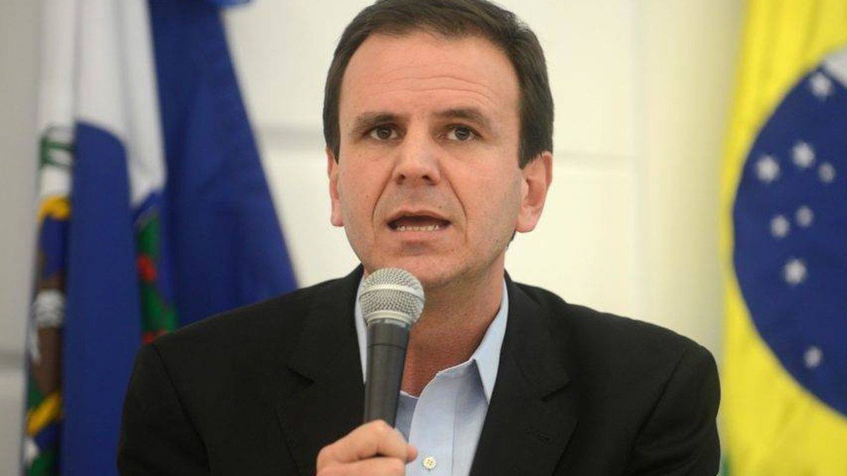 Eduardo Paes falando ao microfone, com a bandeira do Brasil ao fundo, em foto de arquivo
