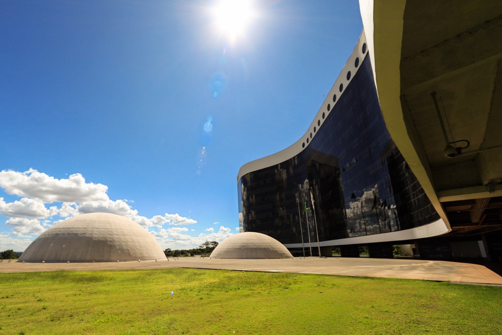Fachada curva de vidro escuro da sede do Tribunal Superior Eleitoral em Brasília, com as duas cúpulas de concreto ao lado e céu azul. Foto de arquivo.