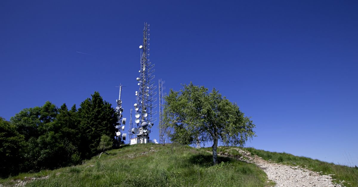 Torres de transmissão de rádio e televisão no alto de uma colina, sob céu azul