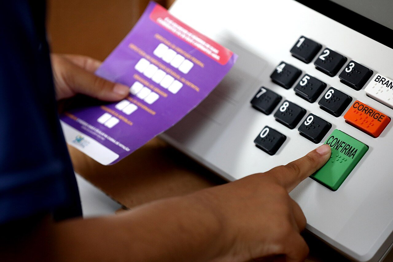 Dedo pressiona a tecla verde Confirma no teclado de uma urna eletrônica da Justiça Eleitoral