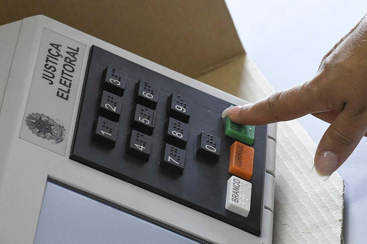 Dedo pressiona a tecla confirma de uma urna eletrônica da Justiça Eleitoral